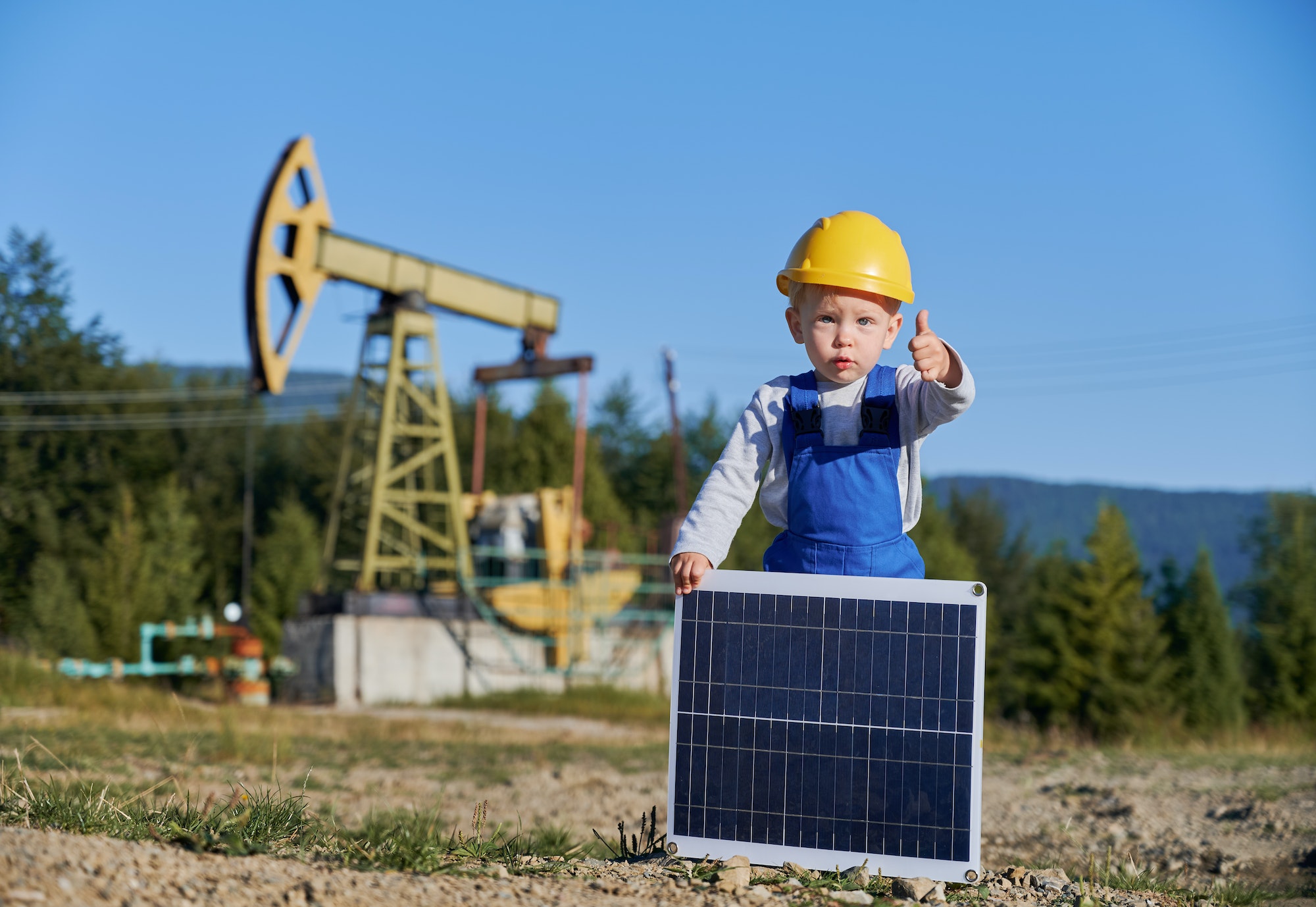 Male child with solar panel showing thumb up against petroleum pump.